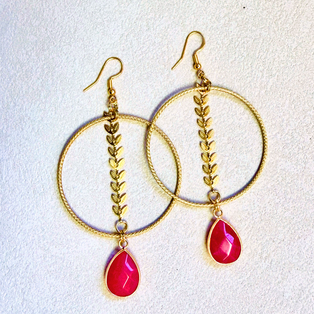 Gold hoop earrings with pink teardrop charms on a light gray background