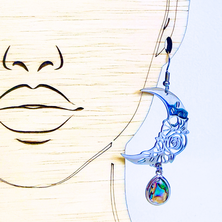 Earring with a crescent moon design and colorful pendant on a stylized face background