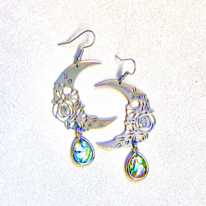 Silver moon-shaped earrings with floral designs and rainbow-colored teardrop charms on a white background.